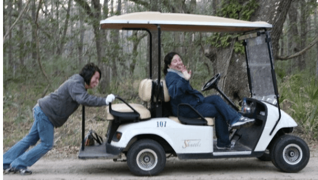 golf cart not work, one lady pushing another in the driver seat