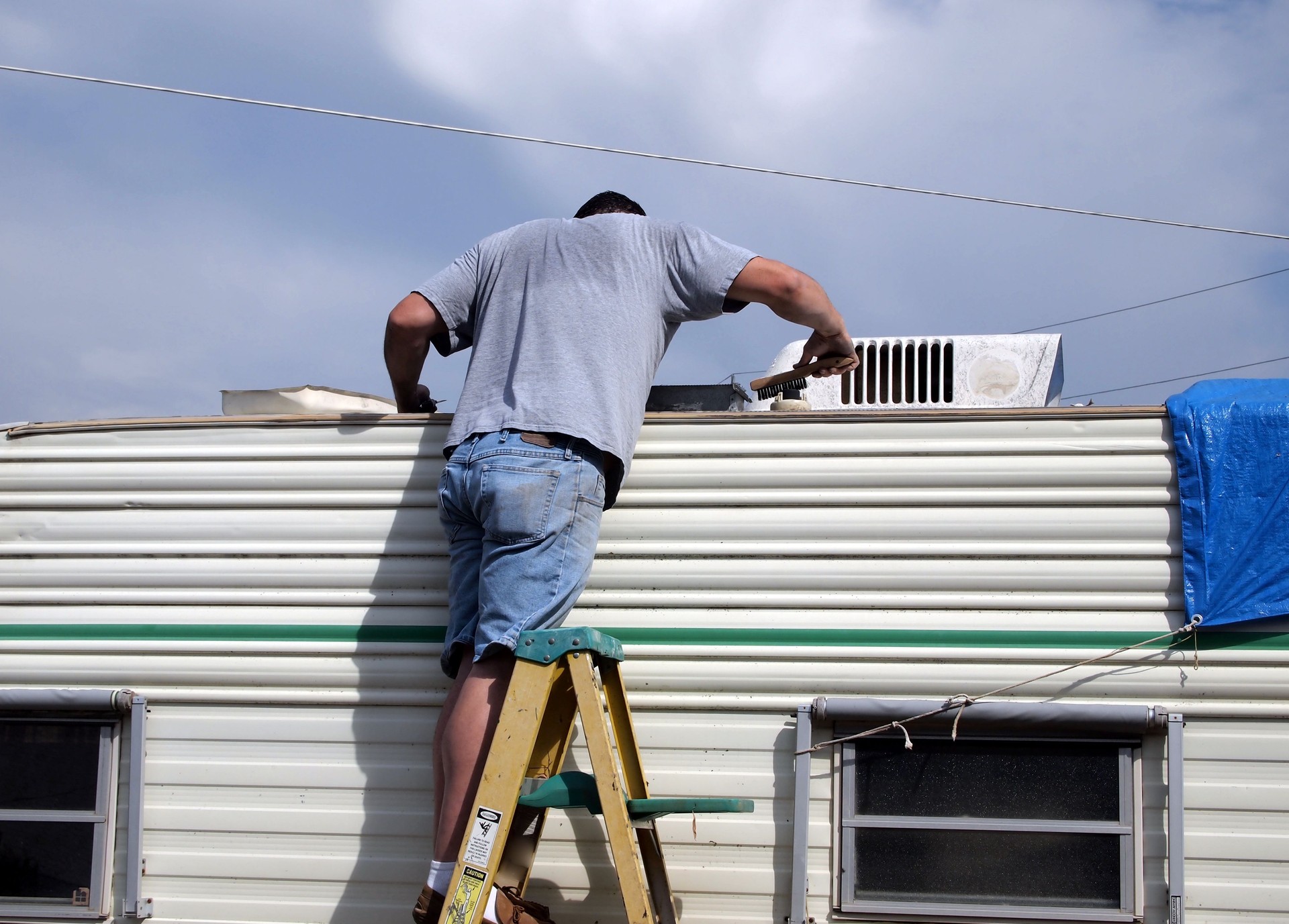 Young man on ladder working on camper roof.